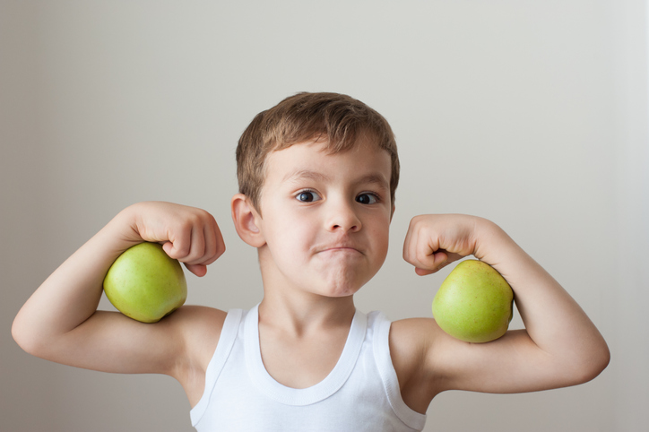 Child flexing his muscles with apples in each arm